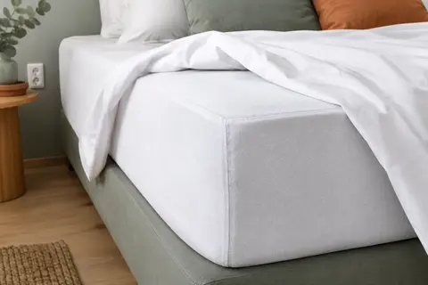 Protège-matelas blanc en Tencel, forme drap-housse, installé sur un matelas dans une chambre claire