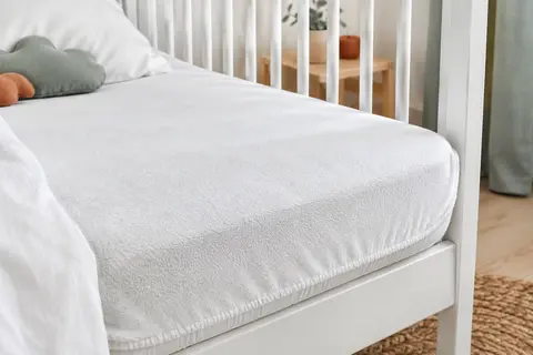 Protège-matelas blanc en bambou ajusté sur un petit matelas de berceau, avec son contour élastiqué visible.