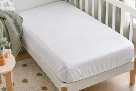 Protège-matelas bébé blanc en polycoton ajusté sur un petit matelas, avec ses coins élastiques visibles.