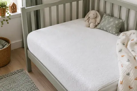 Protège-matelas bébé blanc en bouclette ajusté sur un matelas de lit bébé