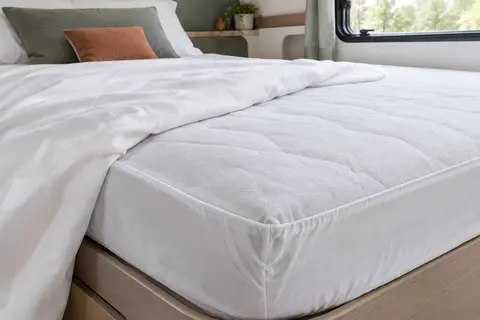 Protège-matelas blanc matelassé ajusté sur un couchage de camping-car, avec son bonnet profond visible.